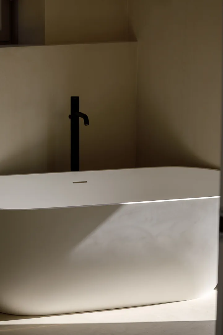 Baignoire îlot blanche, robinetterie noire et matières minérales dans une salle de bains contemporaine