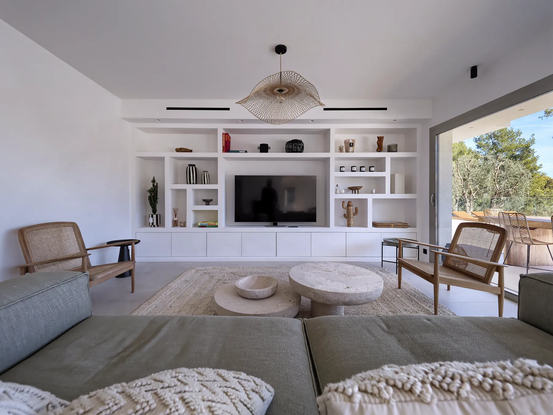 Villa DJORNO : le séjour et son meuble mural sur mesure, tables basses en travertin et fauteuils cannés
