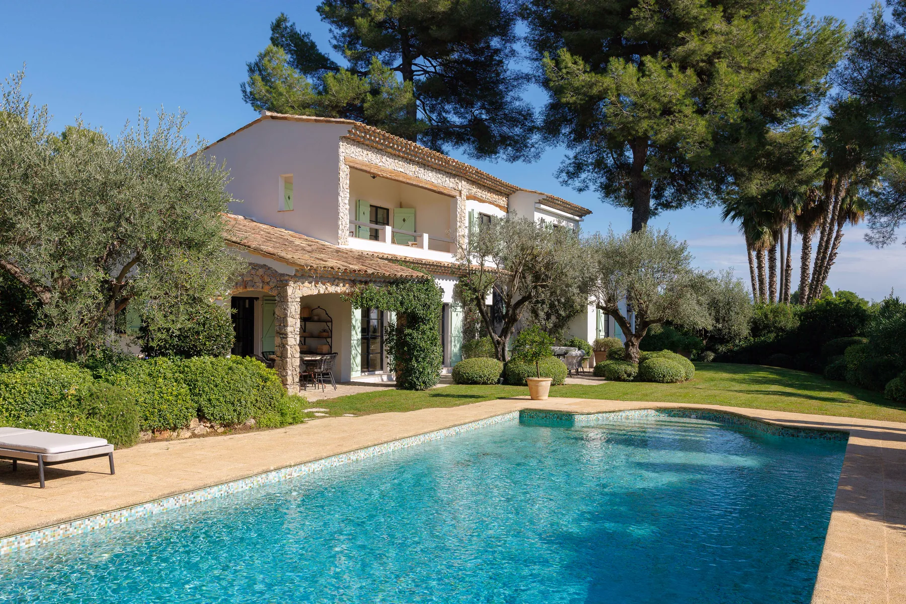 Villa STAN : la bastide aux arcades de pierre et volets vert amande sous les pins, la piscine en mosaïque au premier plan