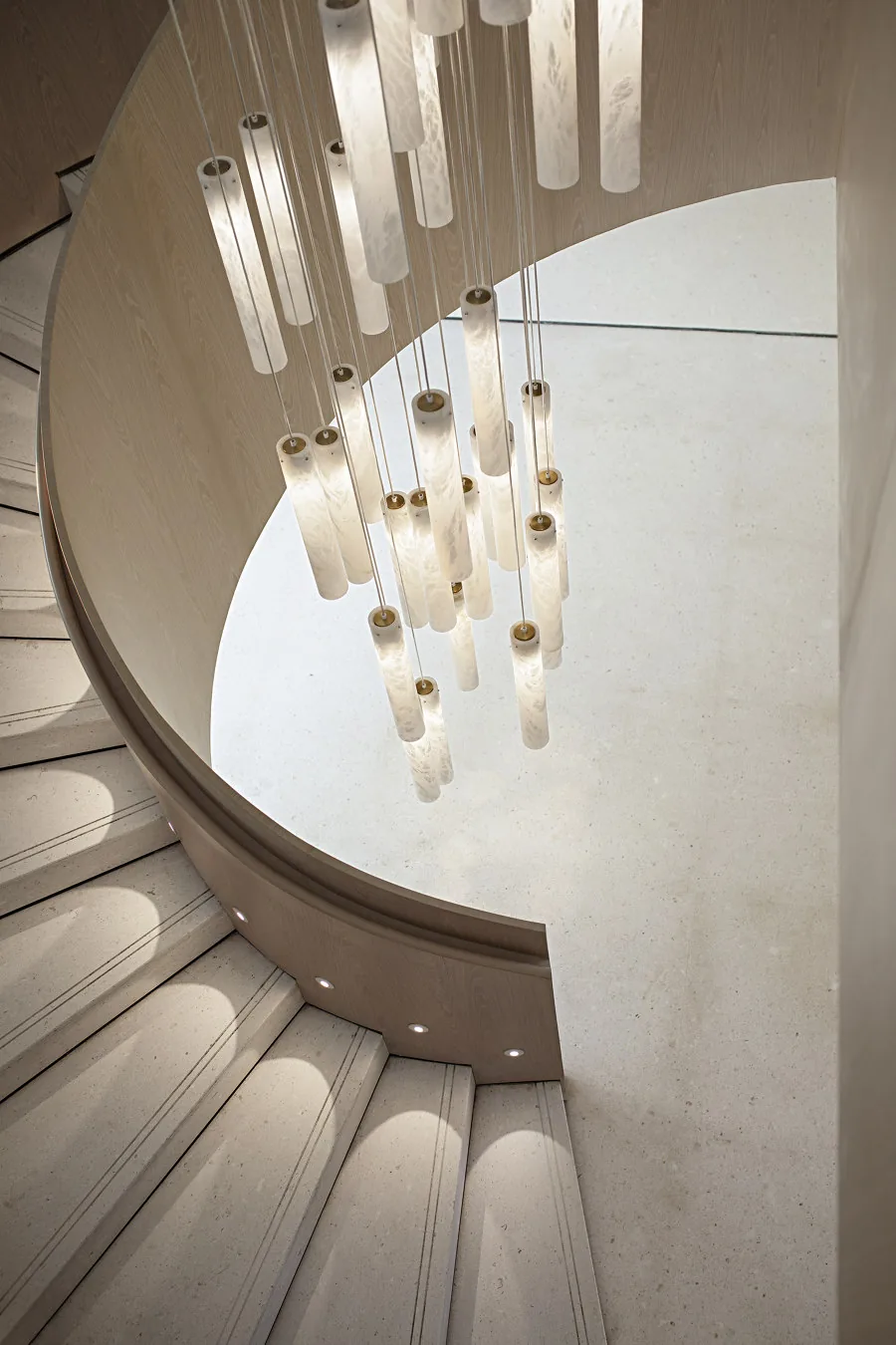 Vue plongeante sur un escalier courbe en pierre claire et une composition de suspensions cylindriques
