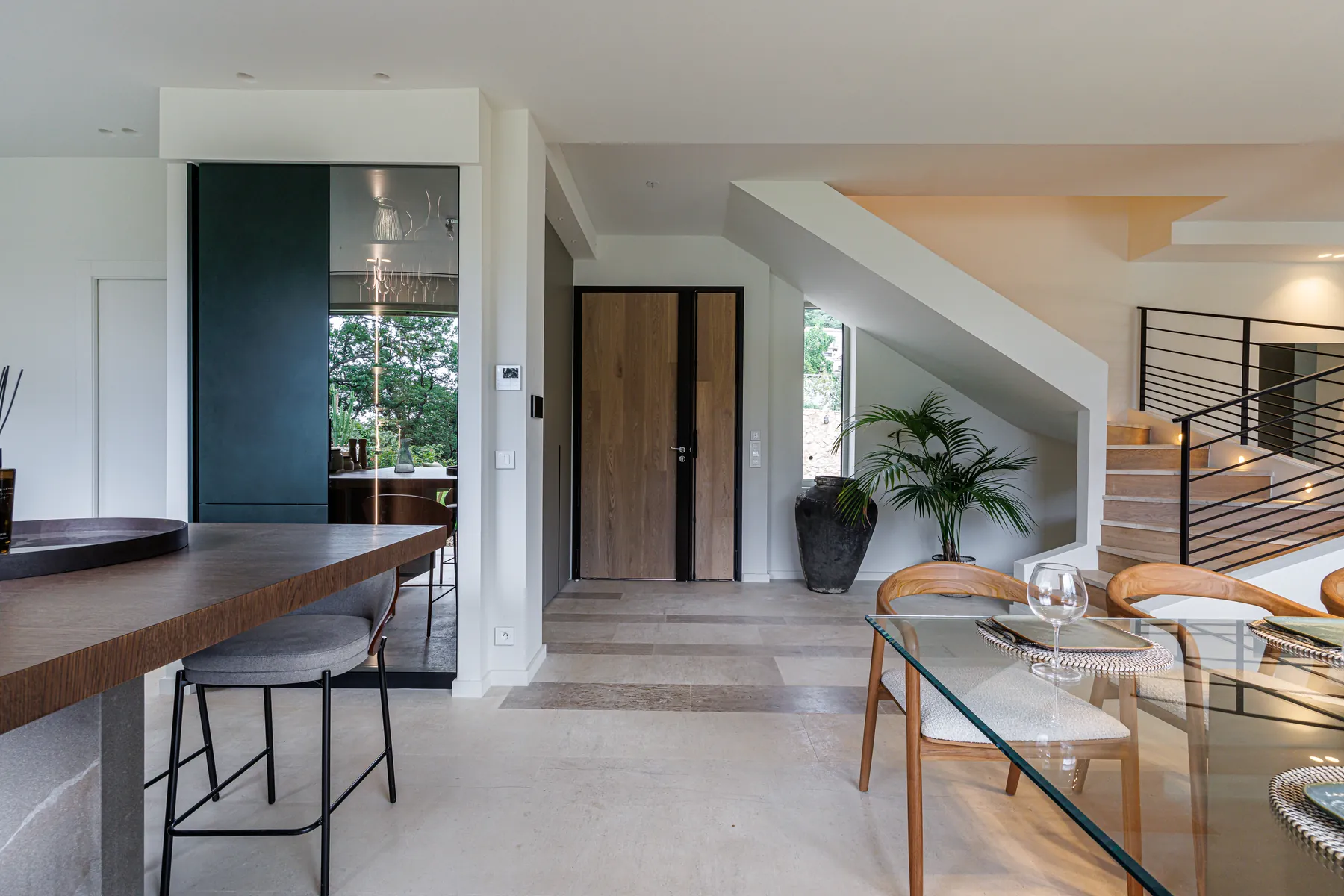 Villa A&G : l'entrée, la porte en chêne, l'escalier à rambarde de métal noir et le bloc cuisine laqué vert